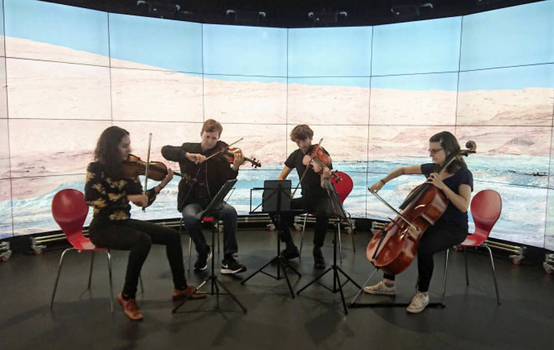 A chamber orchestra playing in front of a digital screen