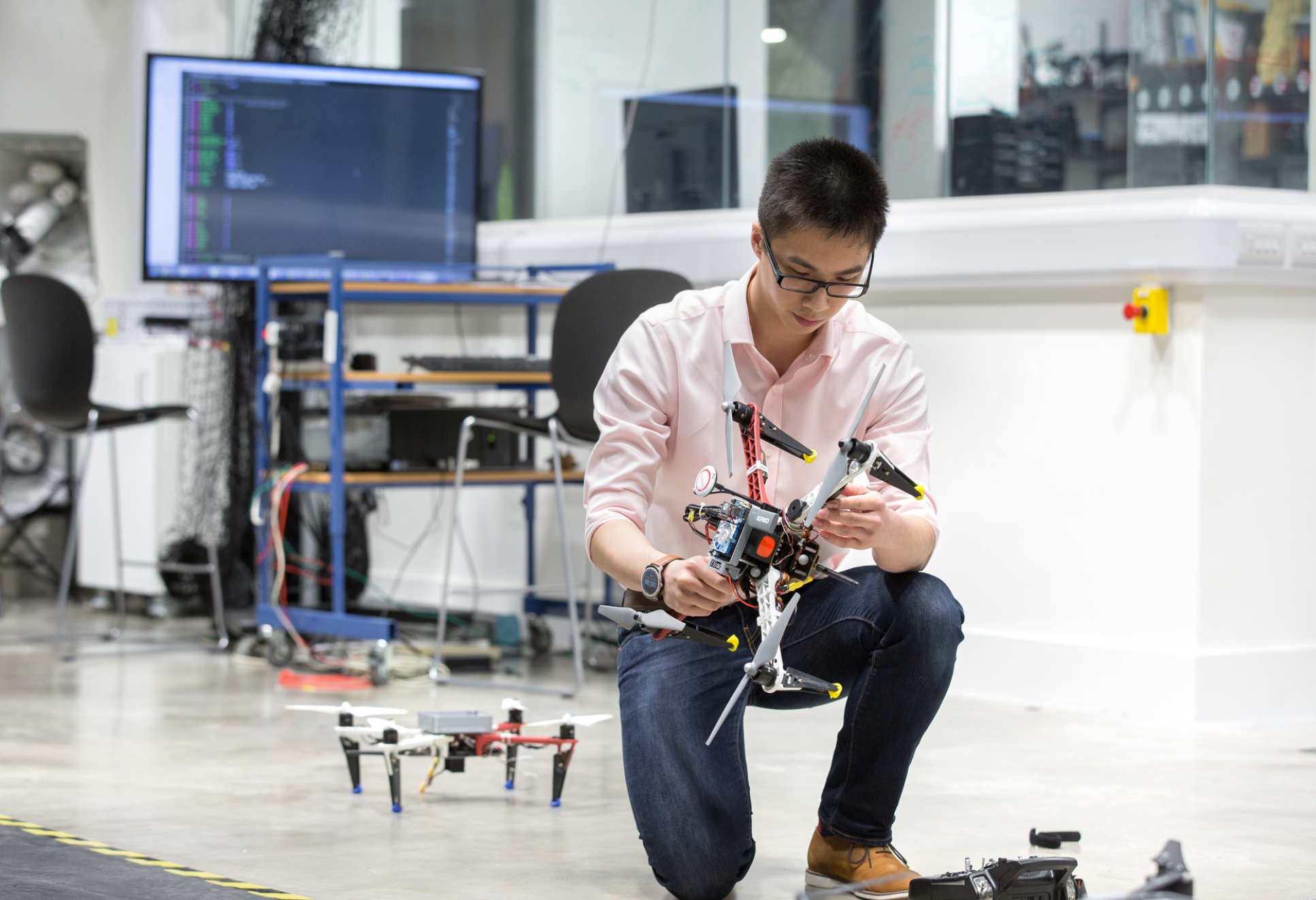 Man crouching and holding a drone, with another behind him