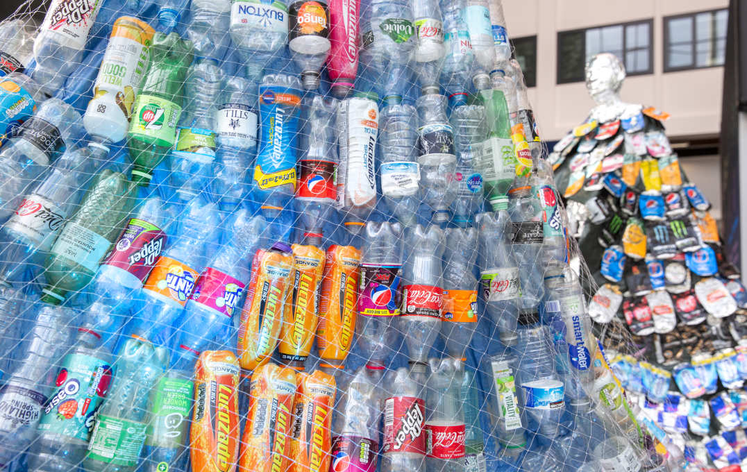 close up of plastic bottles held together by netting. Bottles reado Lucozade, Fanta, Dr Pepper, Diet Coke, Coca cola, Smart water, Buxton