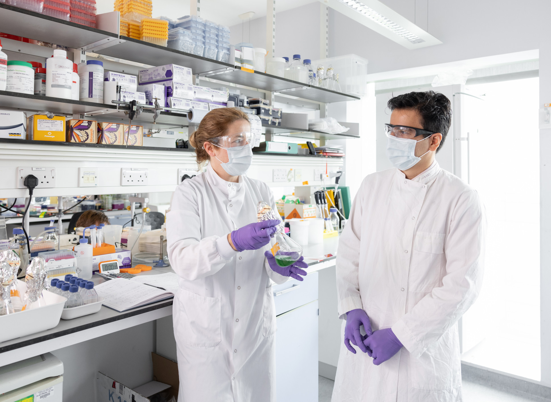 Two scientists having a discussion while holding flasks.