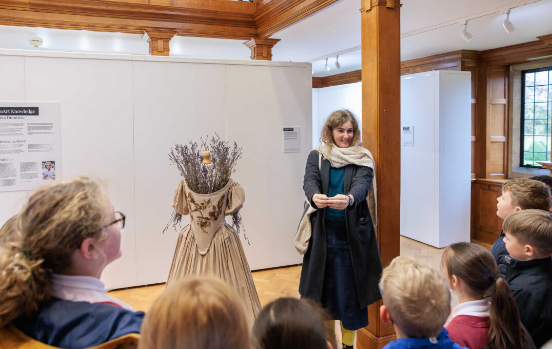 An artist standing with her creation - a dress with flowers coming from where a head should be