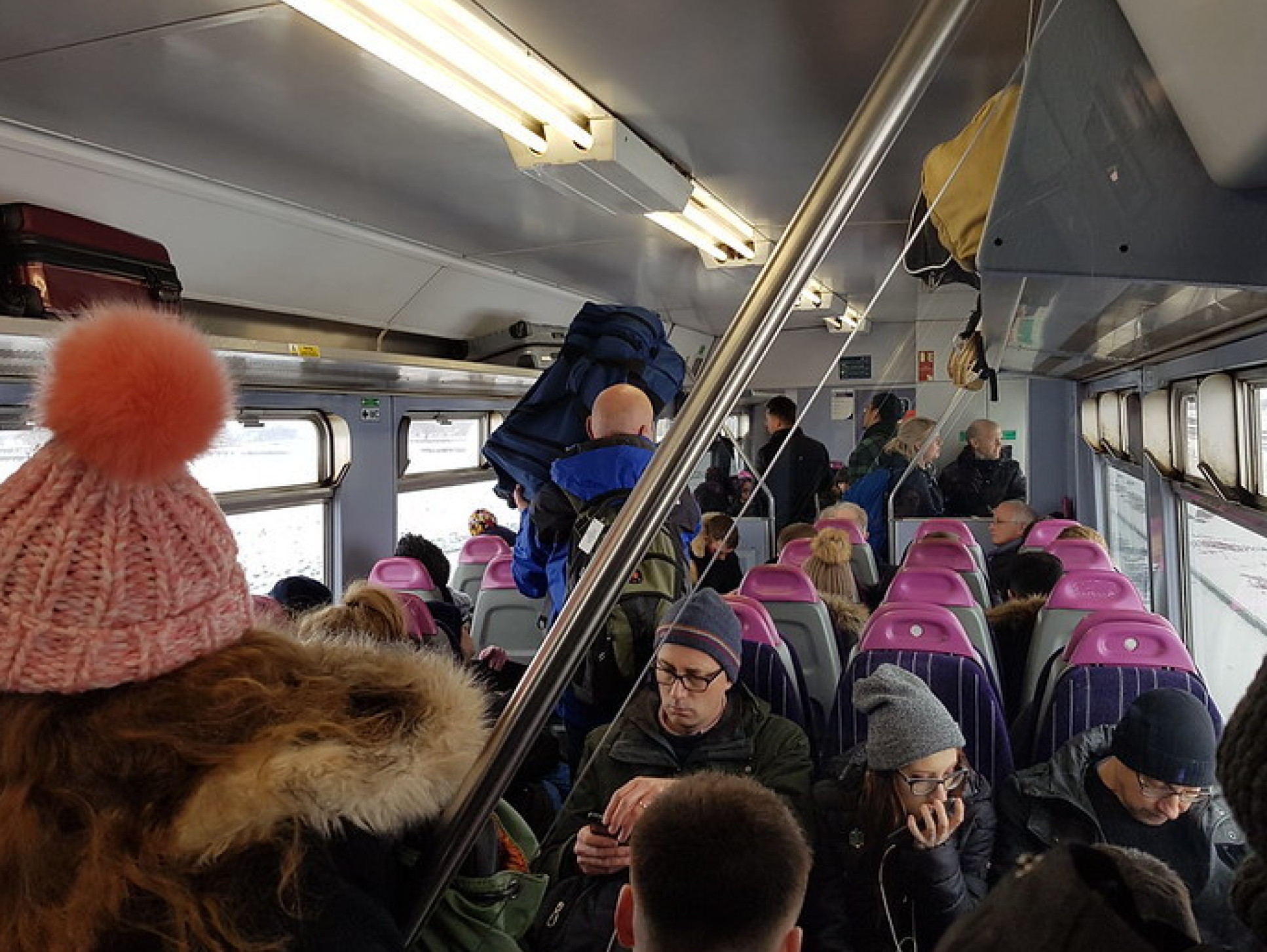 people on a packed UK train carriage, bundled up in coats and hats