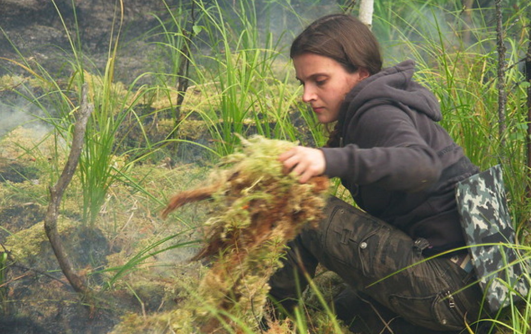 Young woman pulls up undergrowth in smoky forest