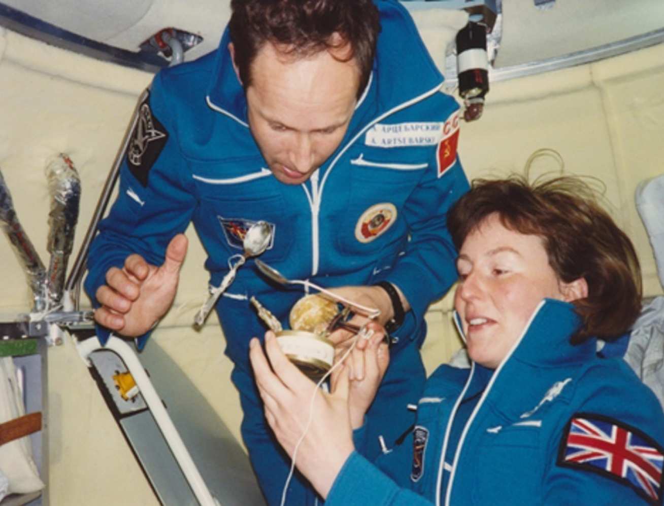 Two people eating from a can on a space station
