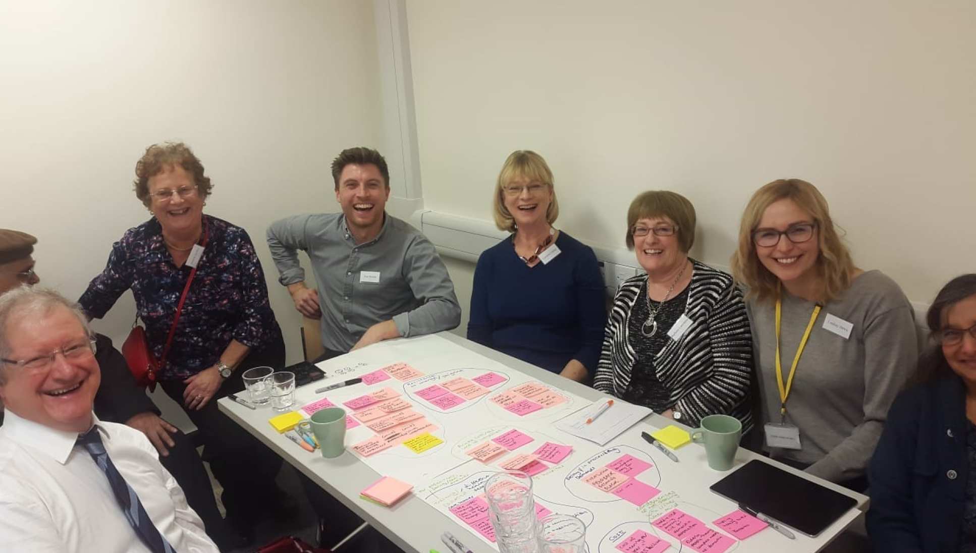 A photograph of members of the workshop sitting around a table with post it notes
