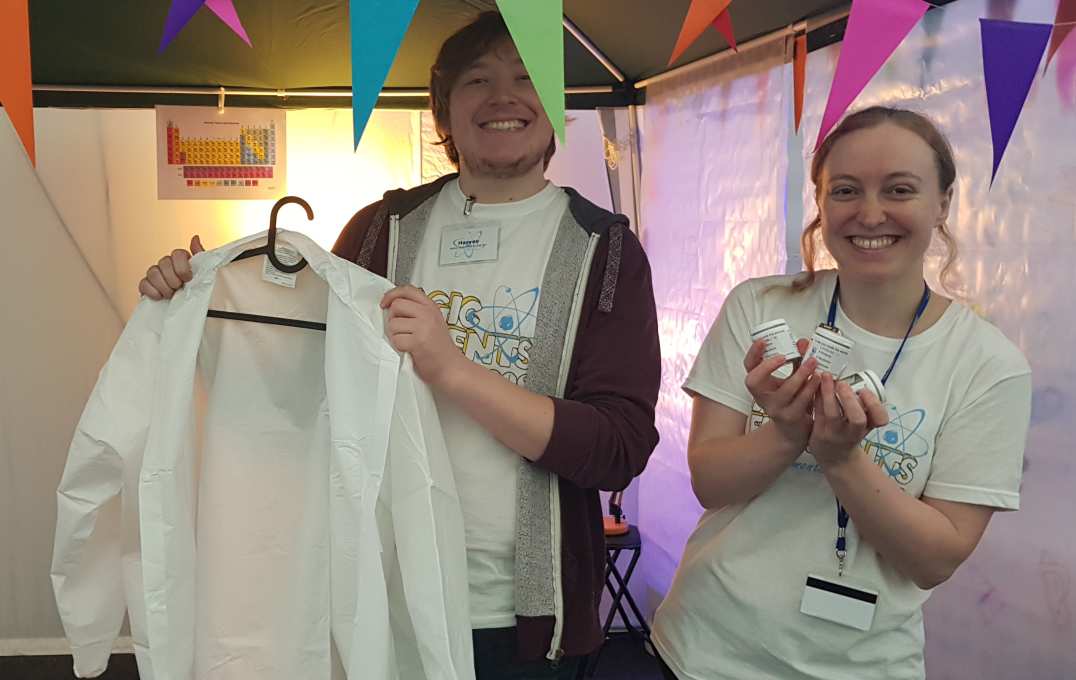 Smiling researchers hold up a child size lab coat and small pots