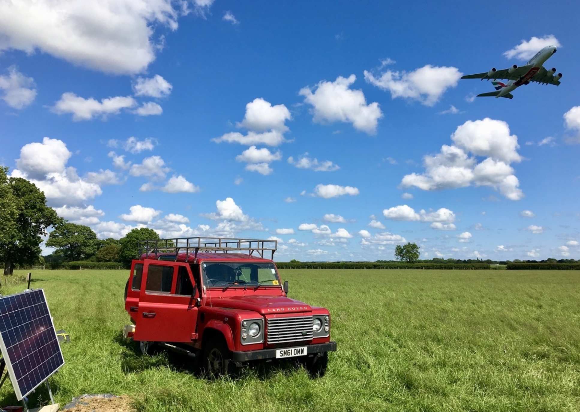Photo showing car in field in foreground and plane taking off in background