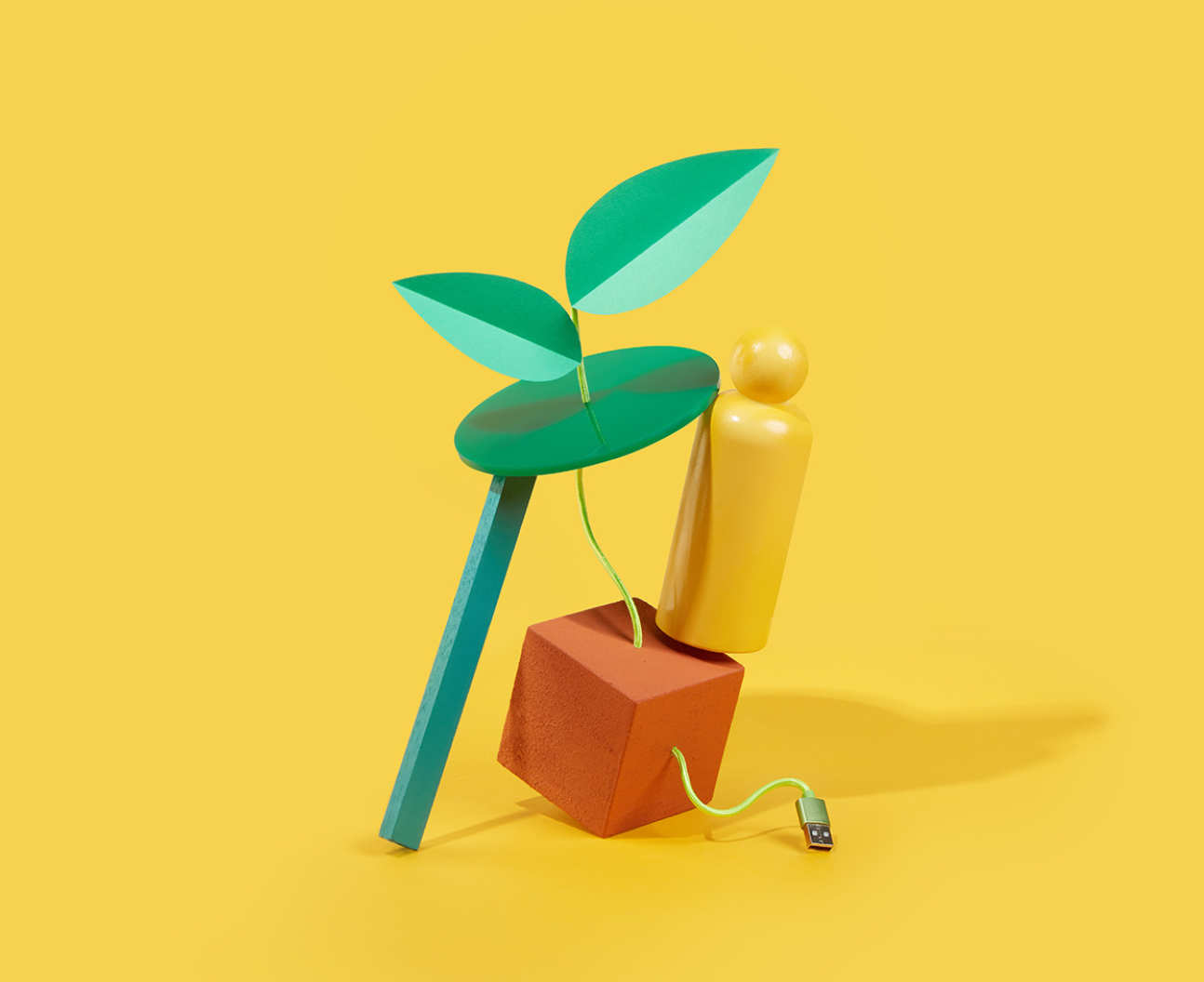 A digital illustration of a green plant connected to an orange cube by a USB cable and a yellow playing piece representing a human form perched on top precariously