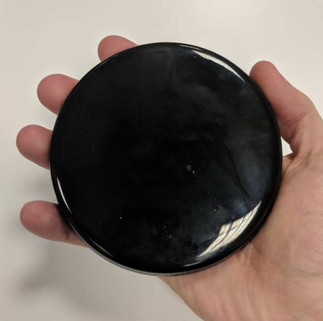 A small black circular puck held in the palm of a hand