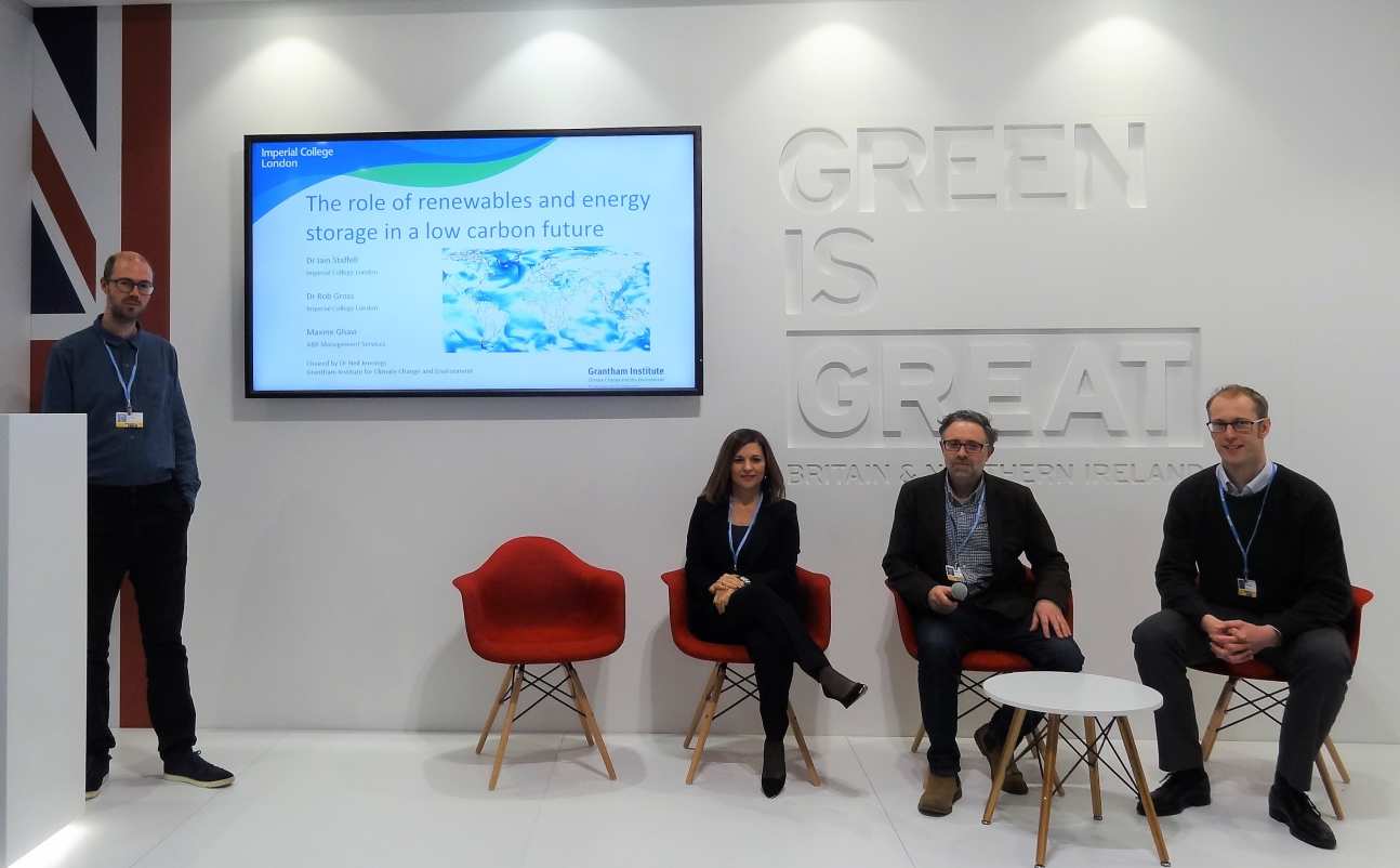 Four people on stage in front of a presentation and a sign that reads "Green is Great"