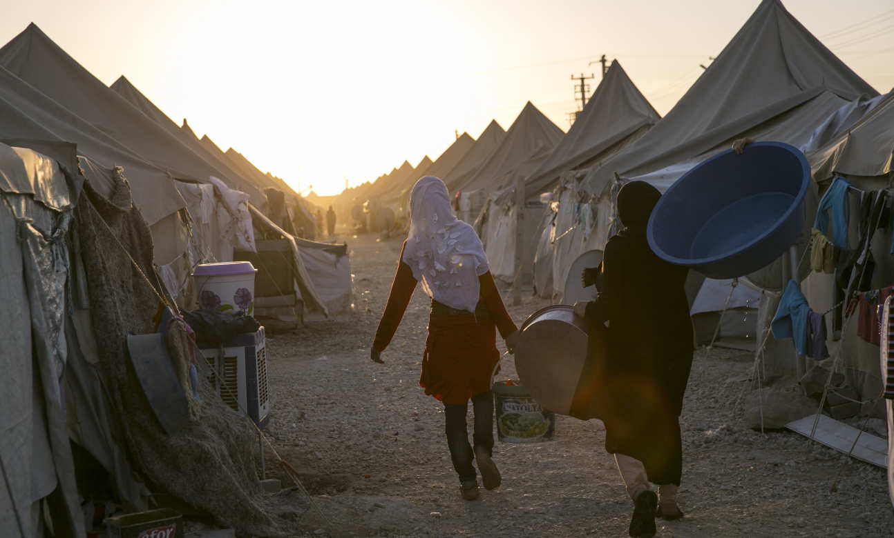 Refugee women carry supplies in a camp