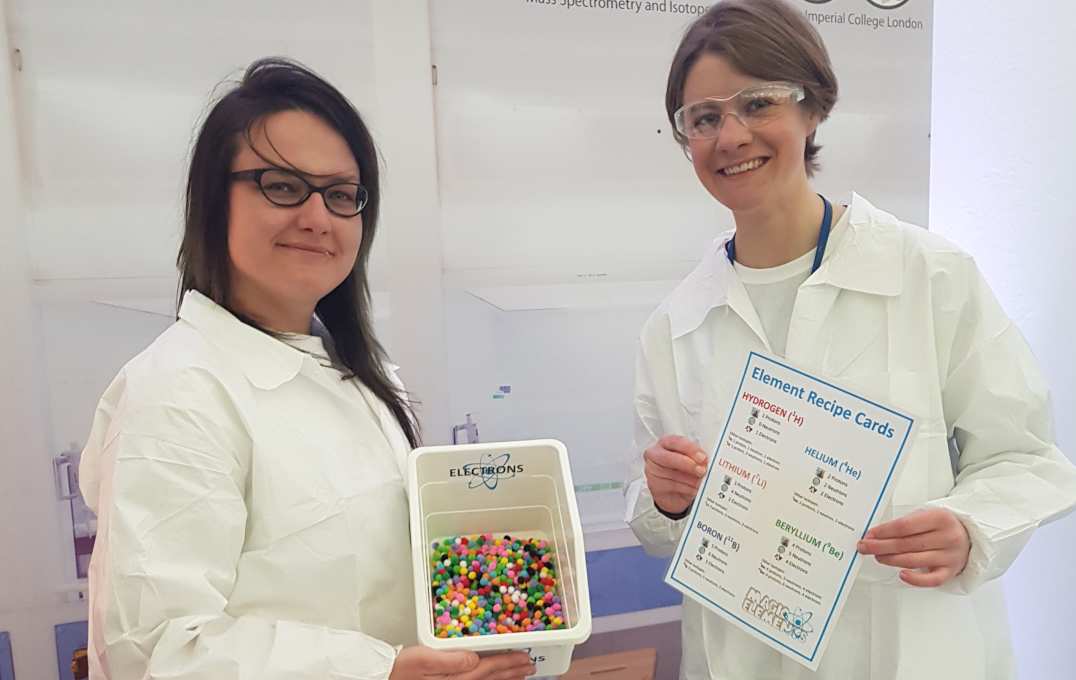 Researchers hold up a white tub of coloured pom-poms and an instruction sheet