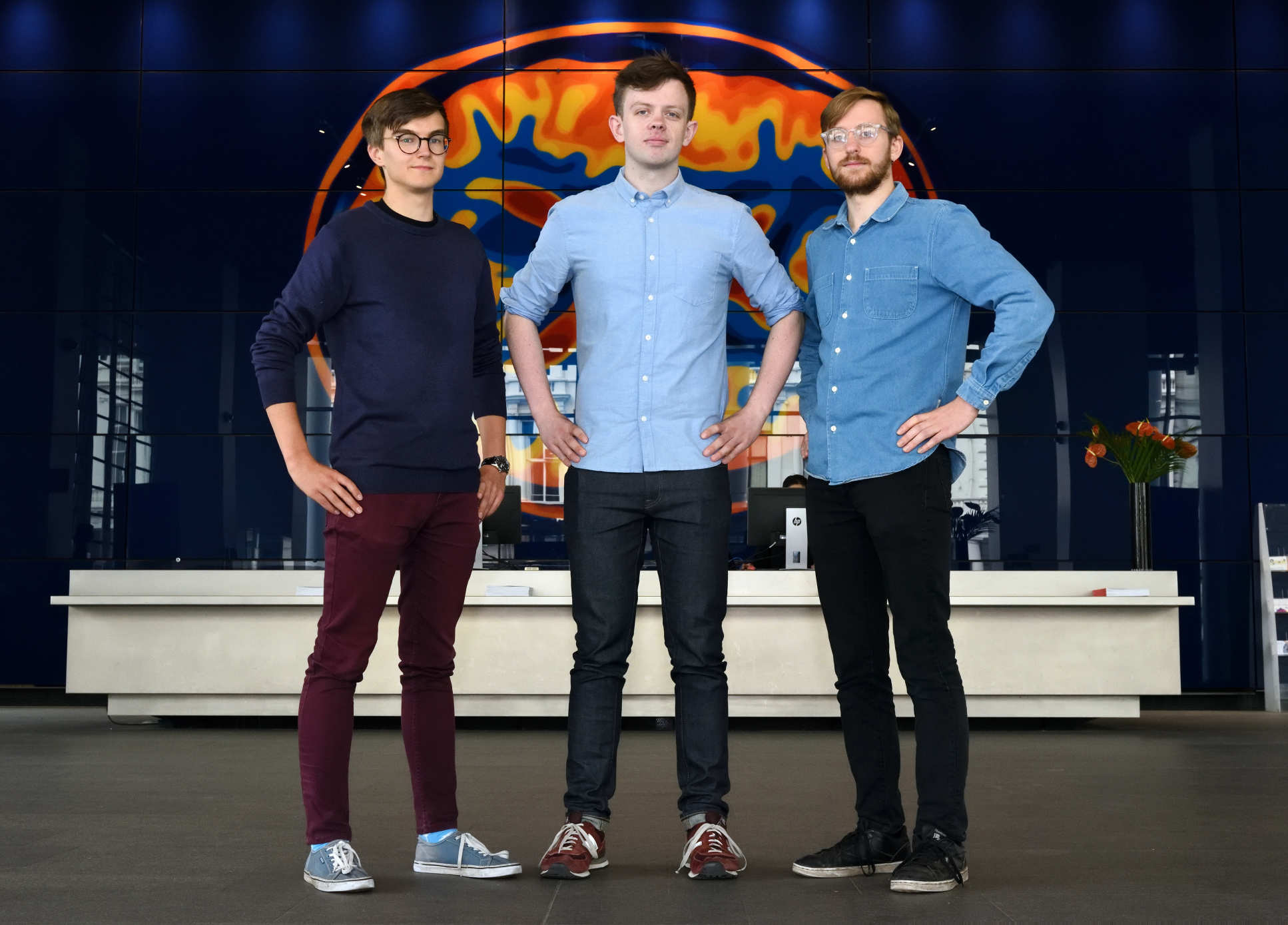 3 young men stand together in group and smile at camera