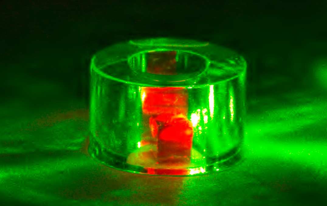 The diamond is held inside a sapphire ring and illuminated by green laser light. The red light is fluorescence from the NV centres.