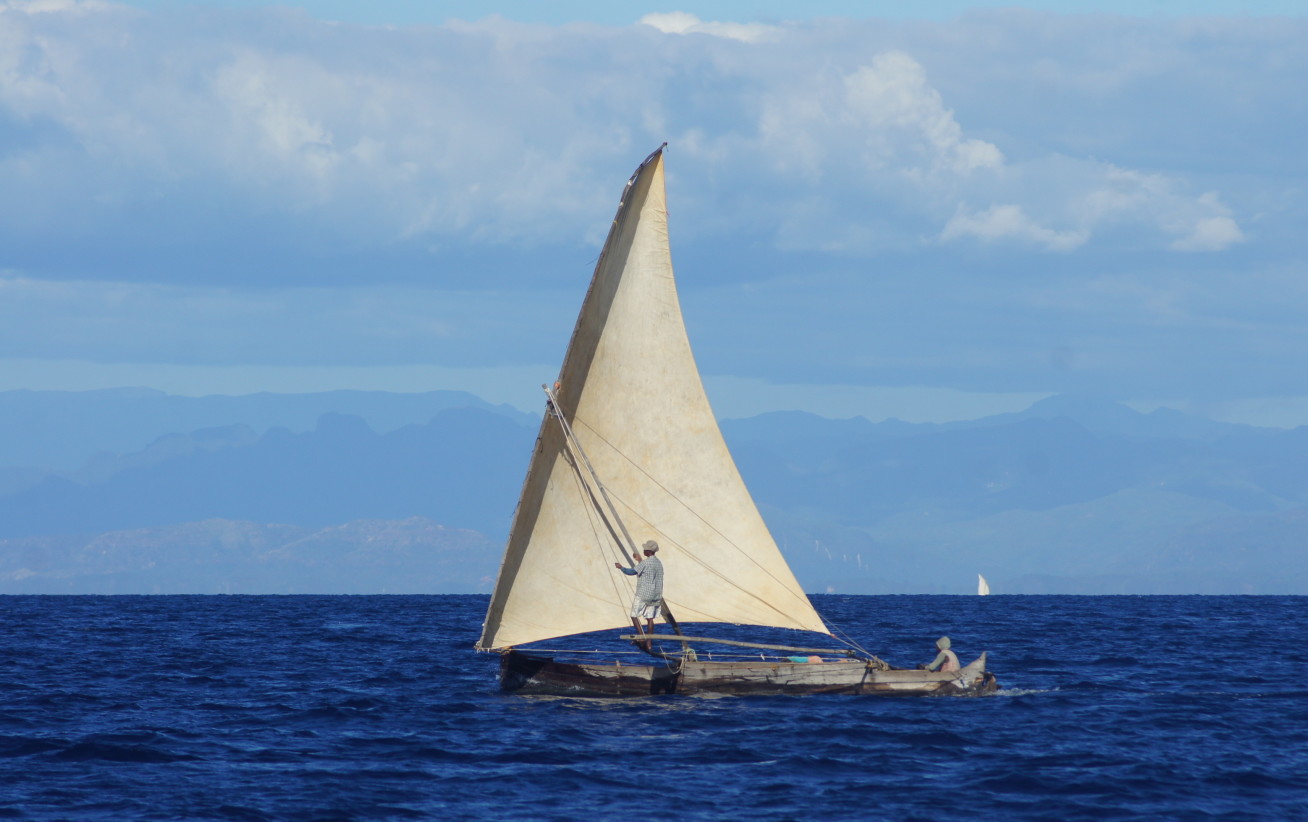 Photo shows small wooden fishing boat with a white sail