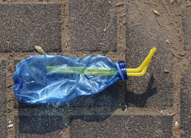 crushed plastic bottle with straws on sandy pavement