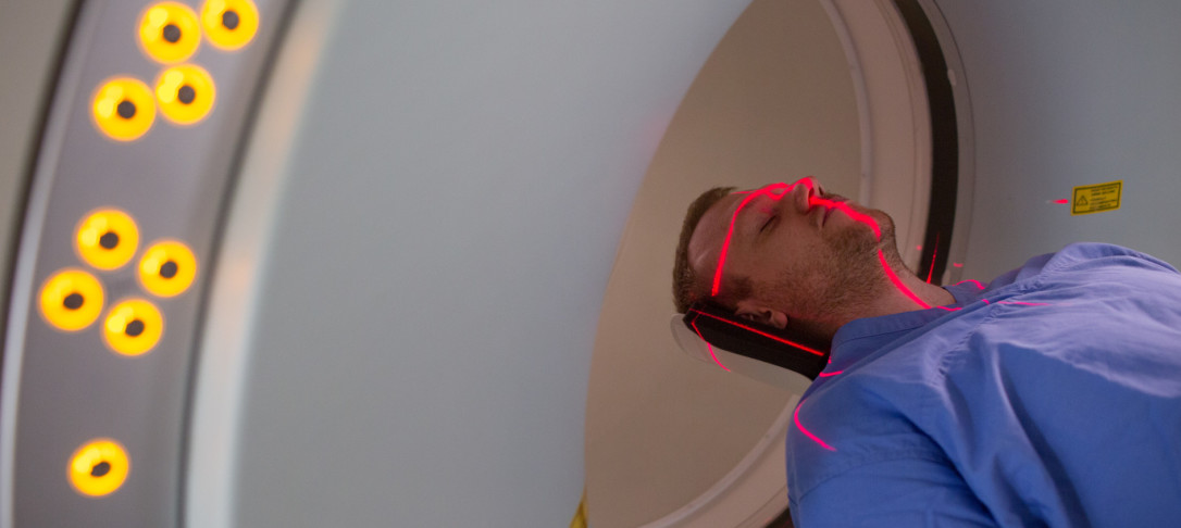A man wearing blue scrubs entering a PET-MRI scanner