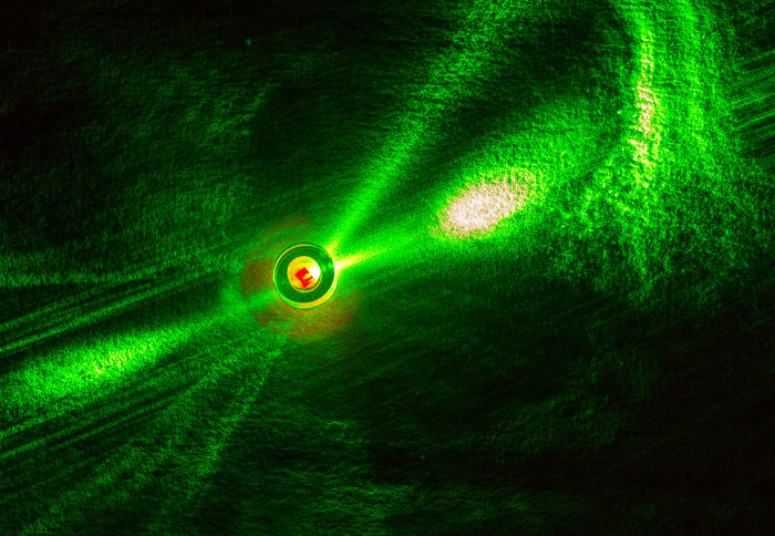 Photo of the diamond held inside a sapphire ring and illuminated with green laser, including red fluorescence from the NV centres.