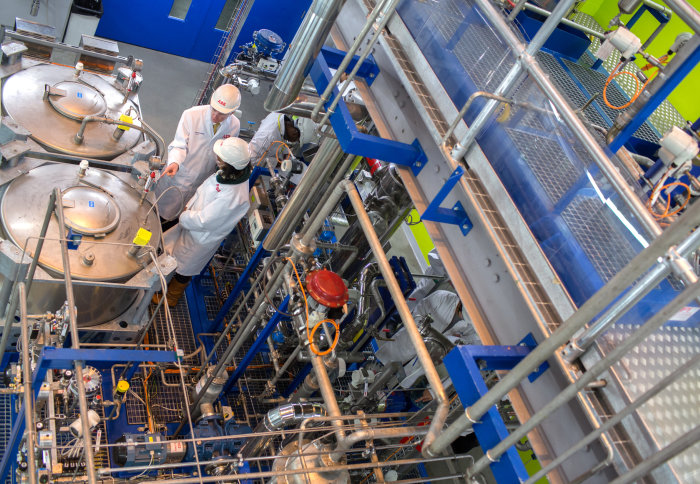 People in white coats and hard hats among pipes and cannisters