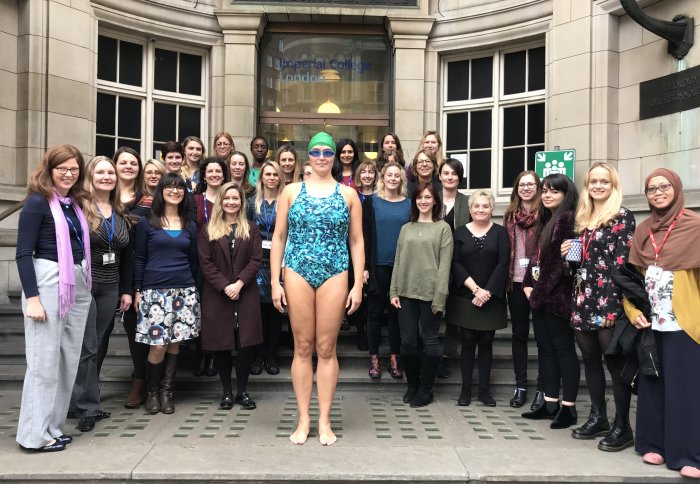 Dr Emma Watson stands in her swimsuit, cap and goggles on the steps on the Royal School of Mines, with 28 women (in clothing).
