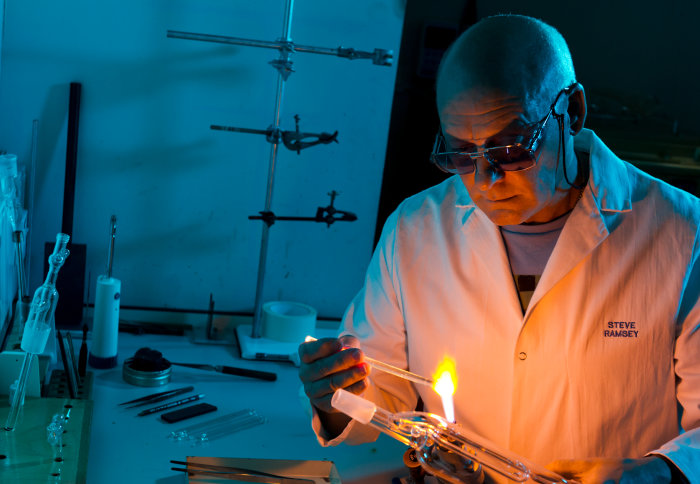 Man holding a small glass tube over a flame in a lab