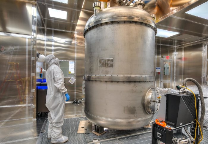 Man in protective gear looking at a large metal cylinder