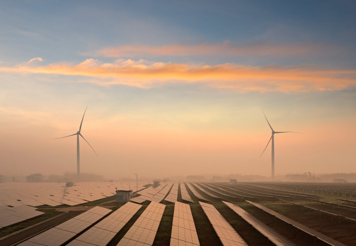 Field of solar panels at dusk with wind turbines in the background