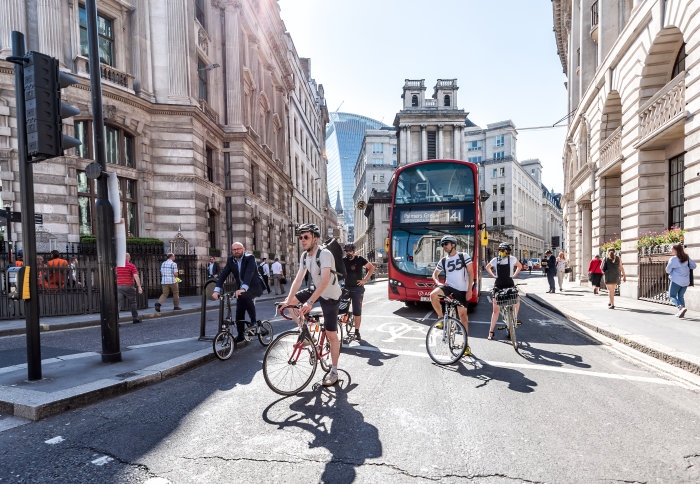 Cyclists waiting at a traffic light in London, with a red bus behind