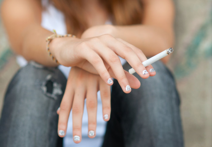 A young woman holds a cigarette in her hand