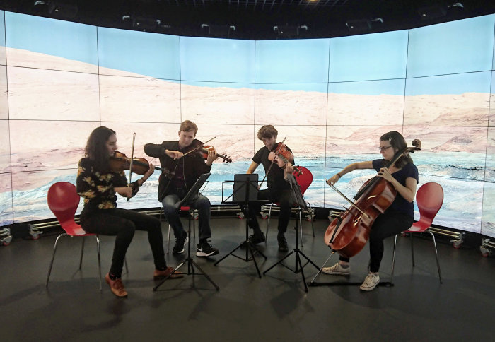 Photo of the Ligeti Quartet practising in Imperial's Data Observatory. A photo taken by the Curiosity Rover is displayed in the background.