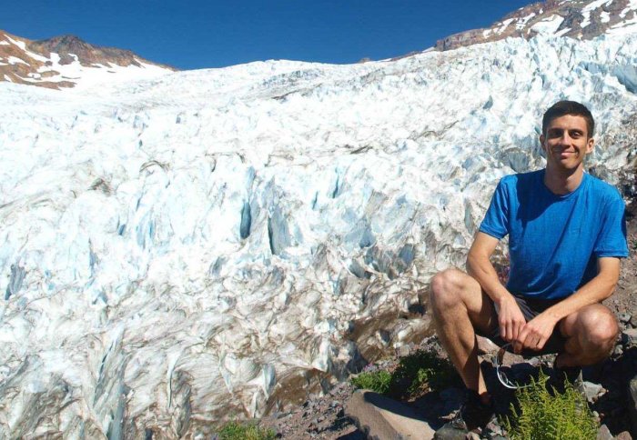 Dr Ceppi crounched down next to Coleman Glacier on Mount Baker in Washington State.