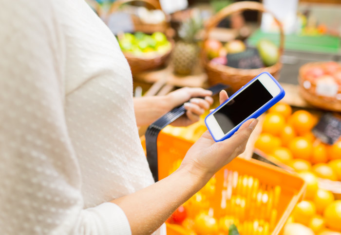 Woman holds smartphone in supermarket in front of fruit and vegetables