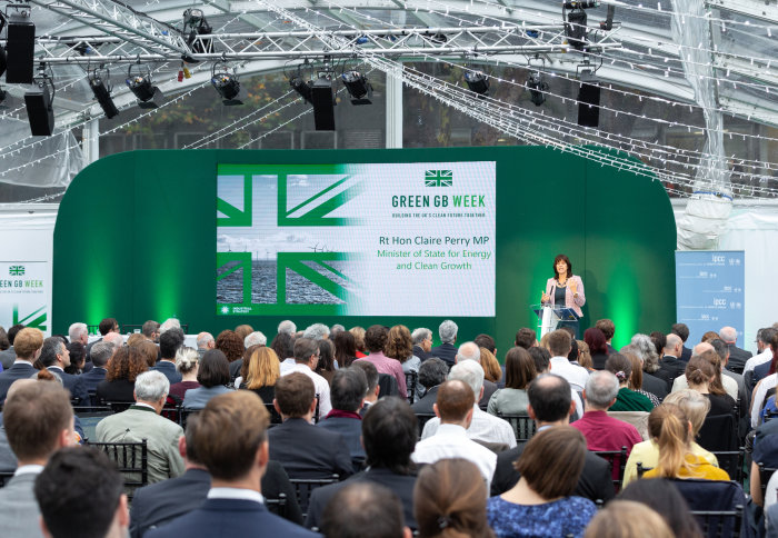 Minister speaks from a green stage in front of an audience of people at the event