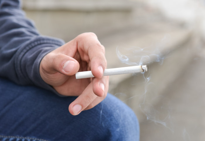 A teenager holds a lit cigarette