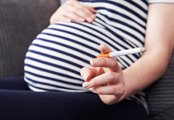 A pregnant woman holds a cigarette