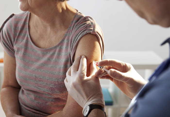 An older lady receives a flu vaccine injection in her upper arm