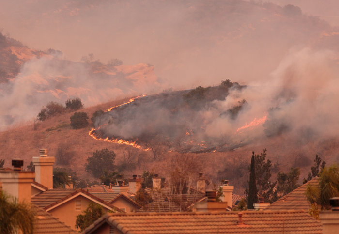 A wildfire spreading on a hill above houses