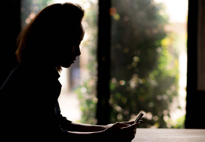 A silhouette of a girl using a mobile phone