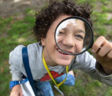 A young boy looks at the camera through a magnifying lens