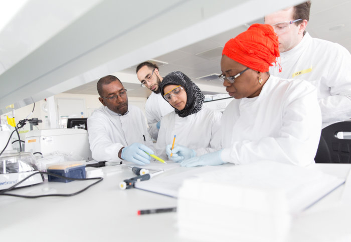 Group of staff in laboratory looking at notepad with lab equipment surrounding them and lab coats on