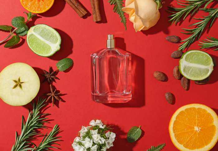 A perfume bottle surrounded by potential ingredients, like orange, rose, lime, vanilla