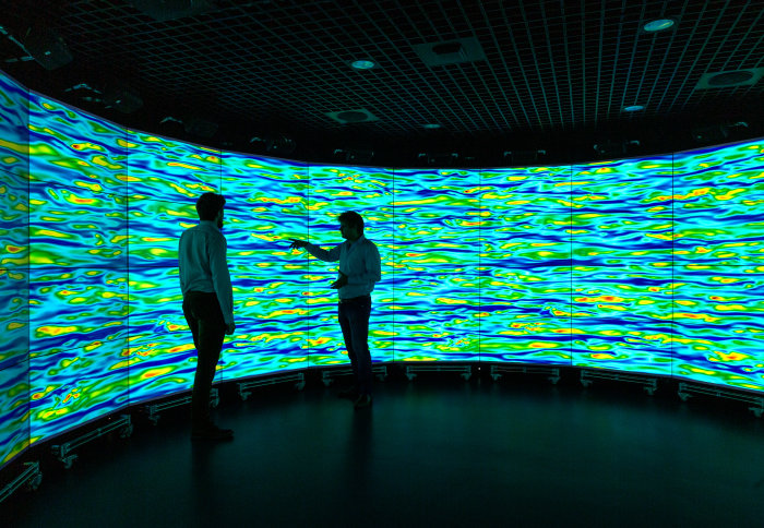 Two people standing in front of wraparound screens showing colourful simulations of turbulent flow