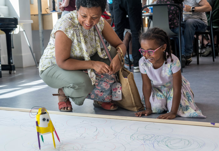 A child and her mother play with a robot