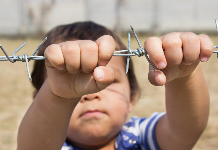 A young child in a minefield holding on to barbed wire