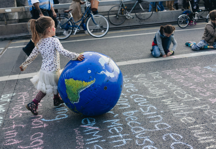 Little girl bounces an inflatable ball printed to look like a globe during climate change protests