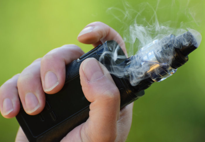 A woman's hand holing a vaping device, with vapour