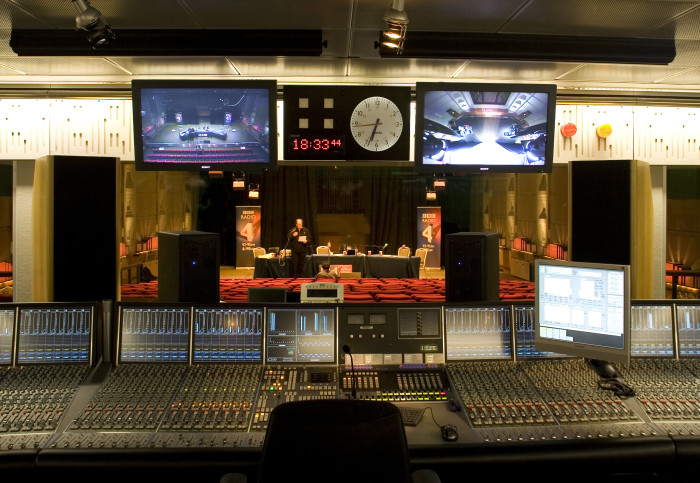 A recording booth, and through the window is the radio gameshow being recorded