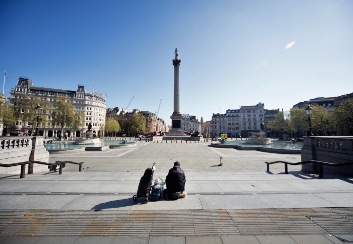 View of Trafalgar Square in central London. Usually packed with tourists and circling traffic, the scene shows one homeless person sitting in the centre. The clear of clouds and aeroplane contrails