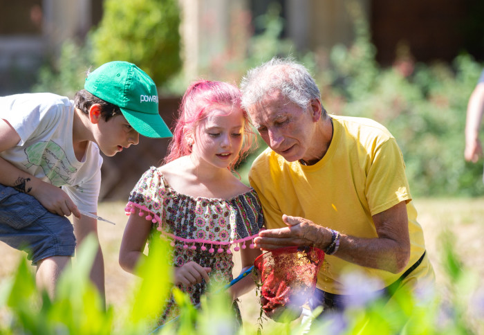 Two children and an adult look at bugs outside