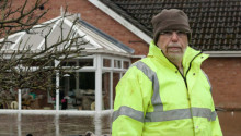 Man in high visibility jacket standing in front of flooded house.